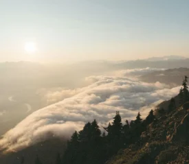 Sunrise casting warm light over mountain ridges and a valley filled with rolling clouds