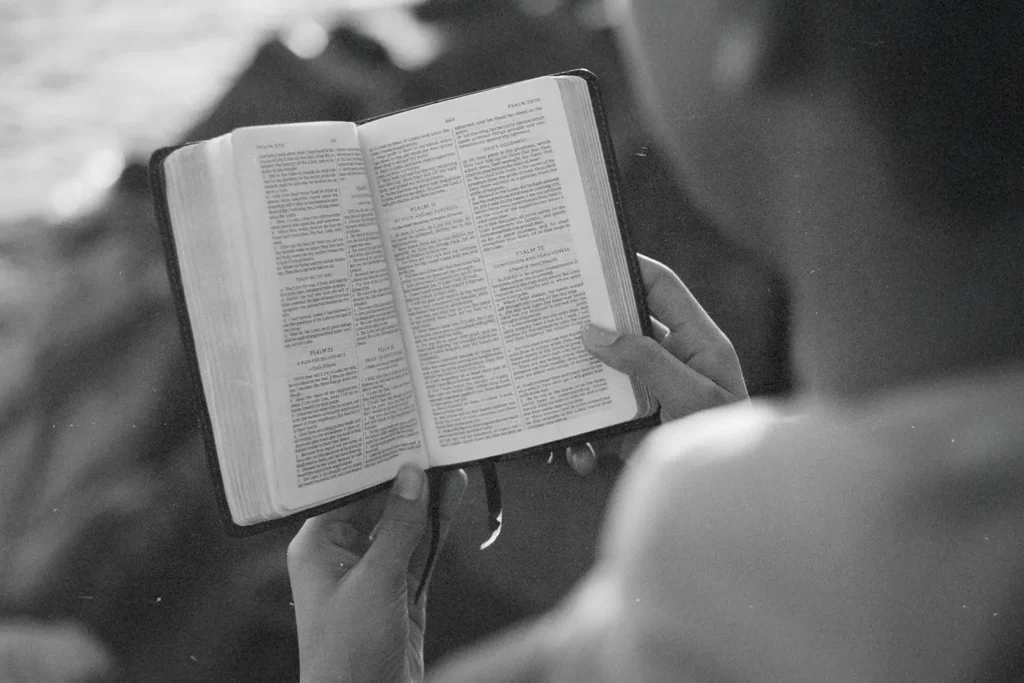 Person holding and reading an open Bible outdoors in soft, natural light