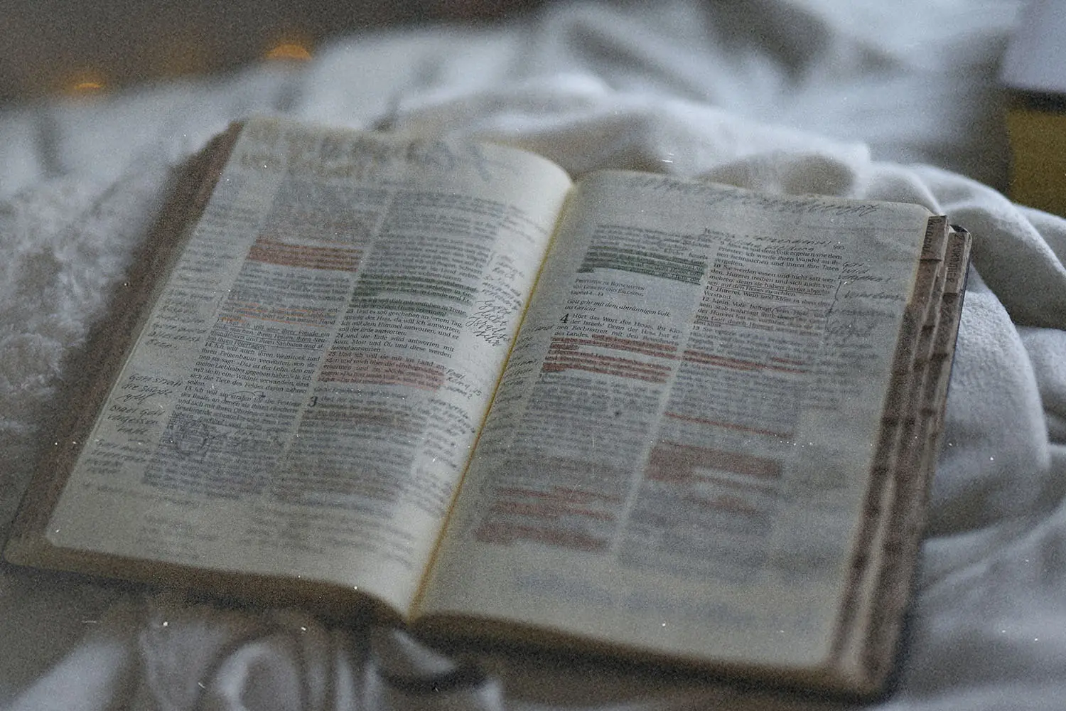 Open Bible with highlighted verses and handwritten notes resting on a soft blanket in gentle, natural light