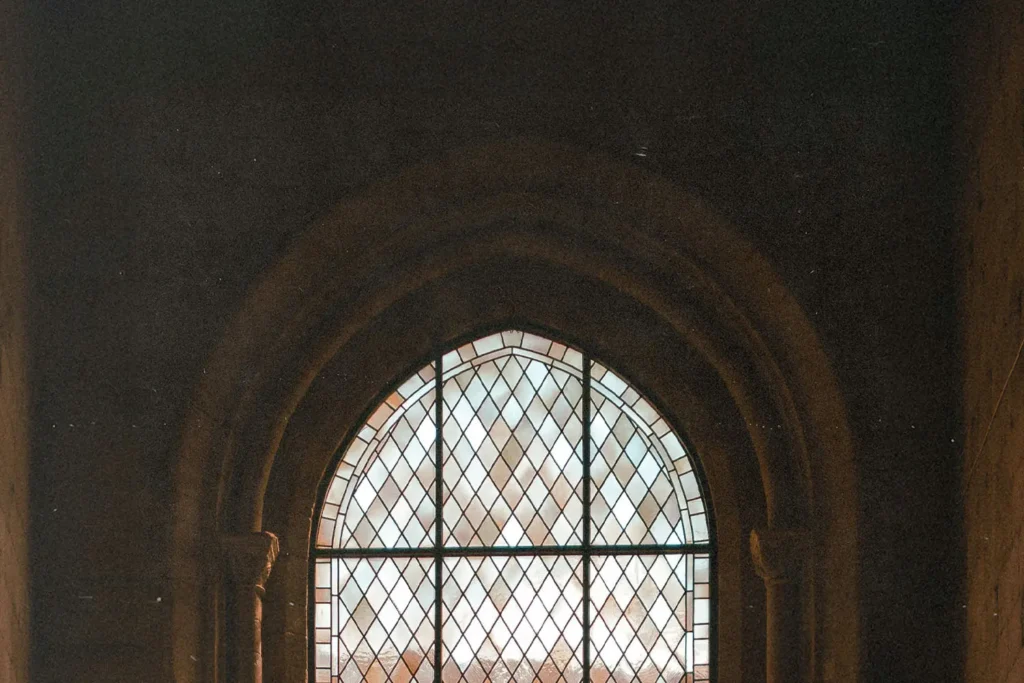 Tall Gothic-style window with geometric glass panes framed by carved stone arches