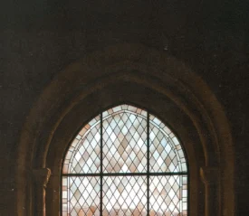 Tall Gothic-style window with geometric glass panes framed by carved stone arches