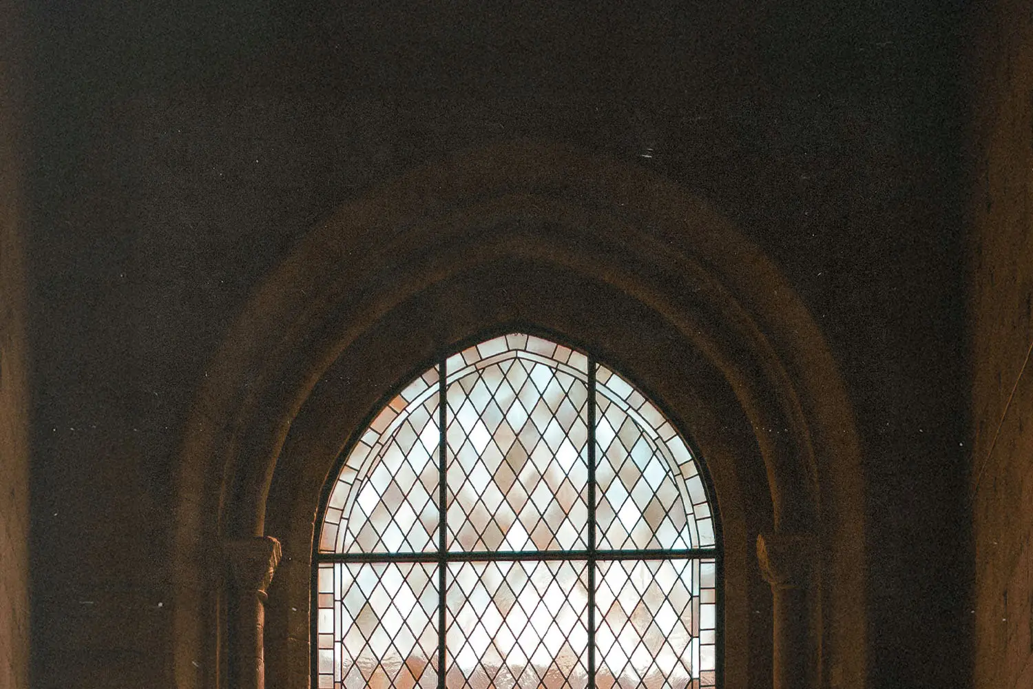 Tall Gothic-style window with geometric glass panes framed by carved stone arches