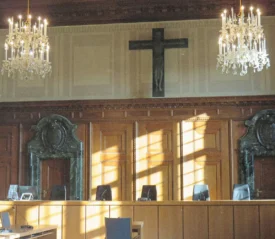 Elegant courtroom with wooden paneling, chandeliers, and a large cross mounted on the wall above the judges’ bench