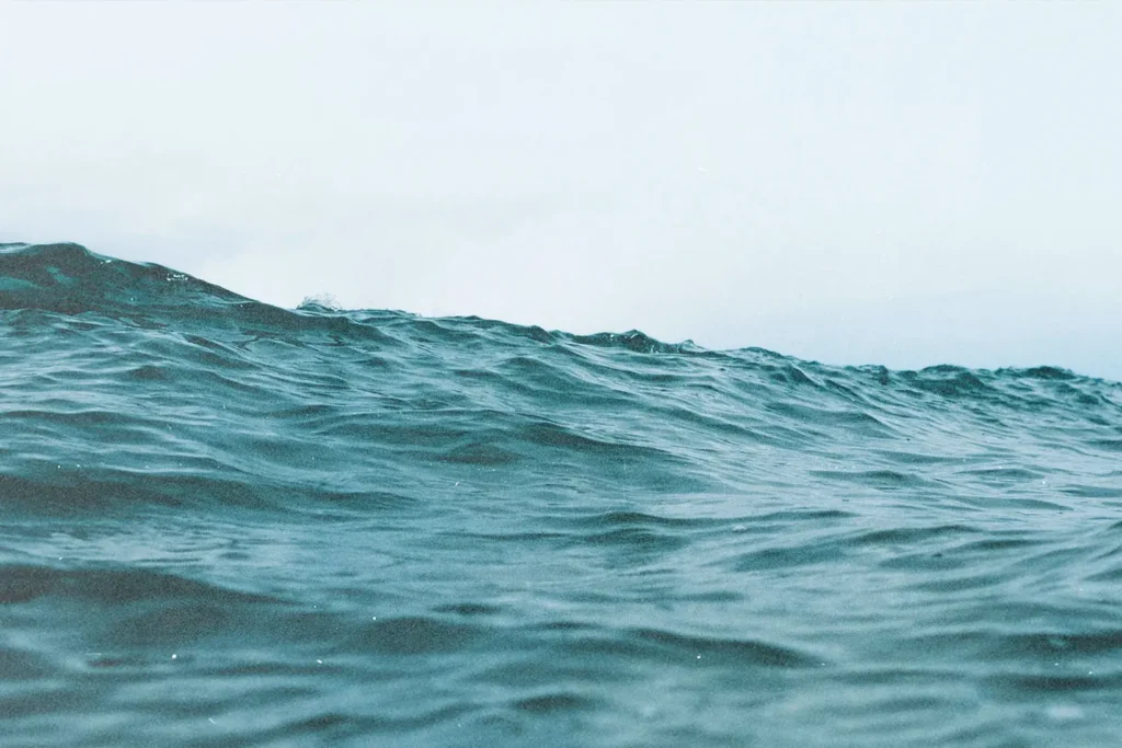 A gentle ocean wave rolls forward beneath a pale, hazy sky