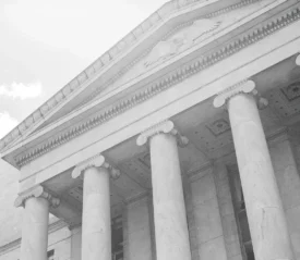 A stone building with tall columns and classical architecture is shown from a low angle, emphasizing its height and symmetry