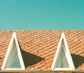 Two triangular attic windows on a red shingle roof beneath a clear blue sky