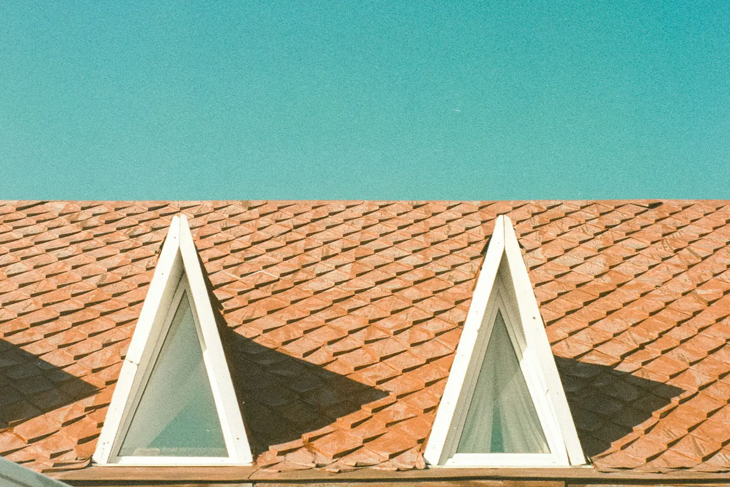 Two triangular attic windows on a red shingle roof beneath a clear blue sky