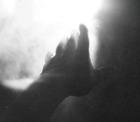 Hand reaching toward a bright light surrounded by soft, glowing mist in a black‑and‑white scene