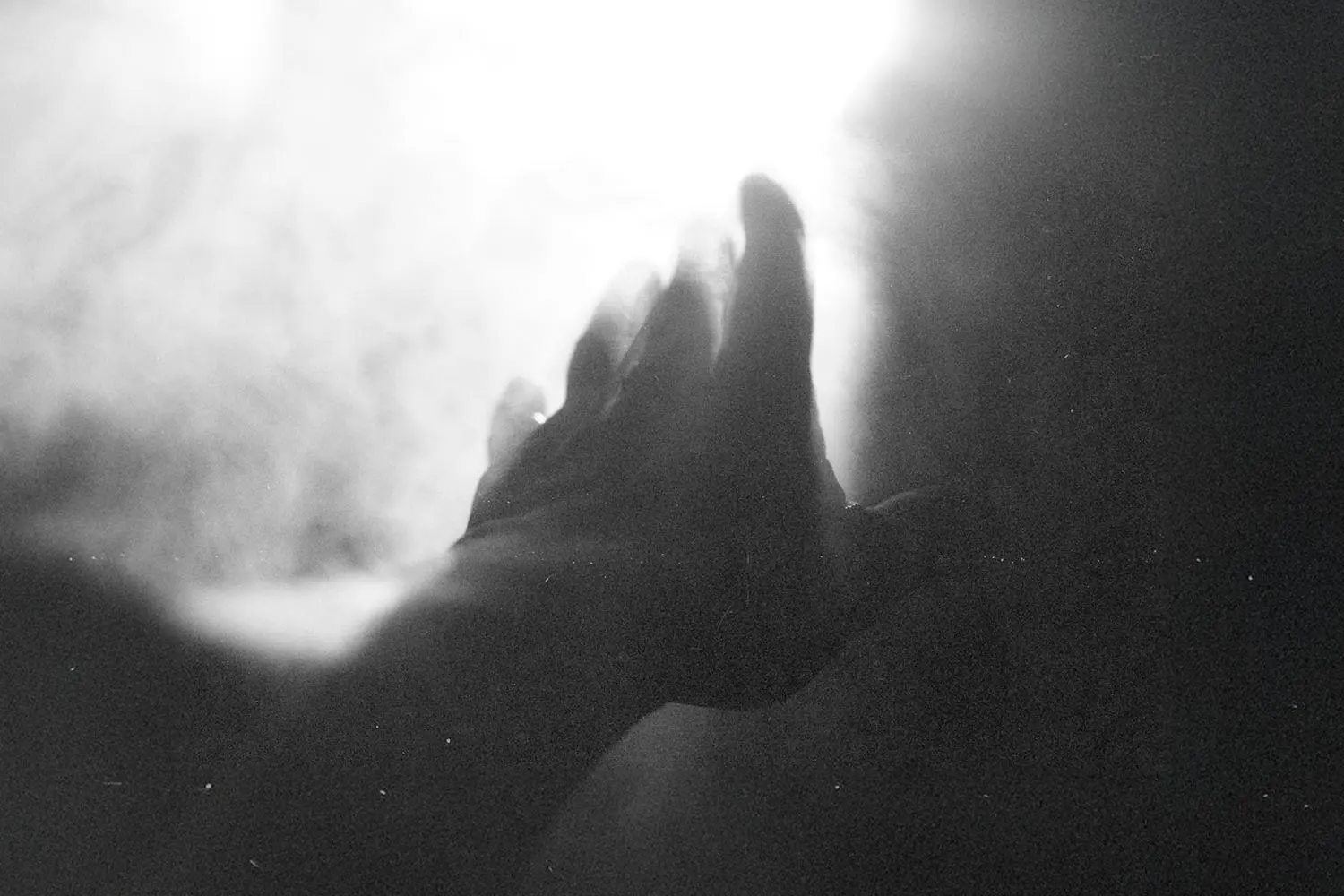 Hand reaching toward a bright light surrounded by soft, glowing mist in a black‑and‑white scene