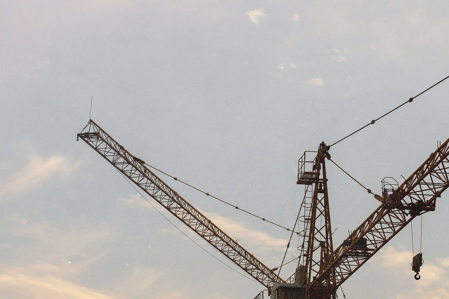 Construction cranes silhouetted against a soft evening sky with light clouds