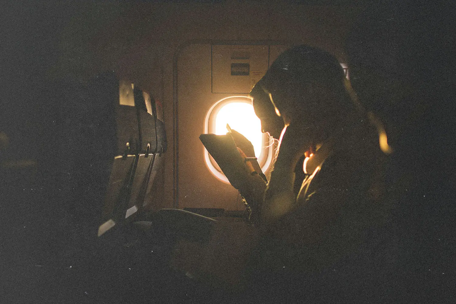 A person sits on an airplane, reading with warm sunlight streaming through the window beside them