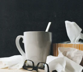 White mug, tissue box, and scattered tissues arranged on a table with a dark background