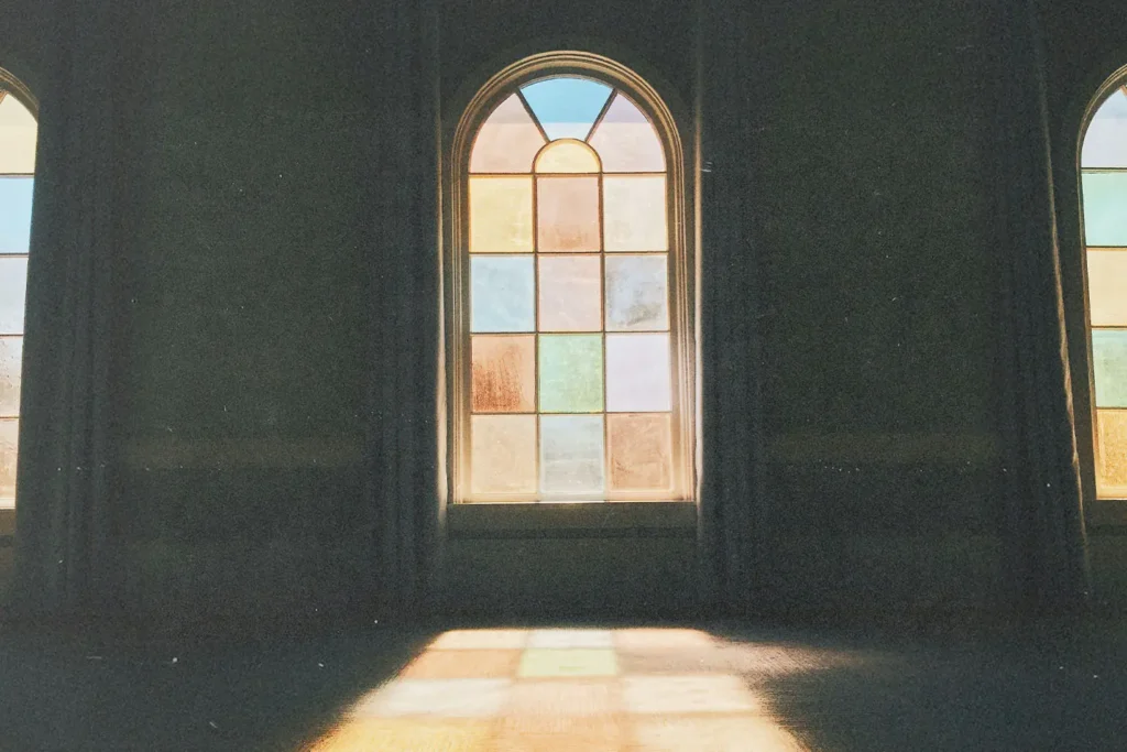 Sunlight shining through tall stained‑glass windows inside a dimly lit room