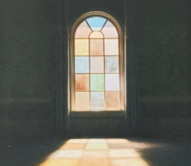Sunlight shining through tall stained‑glass windows inside a dimly lit room