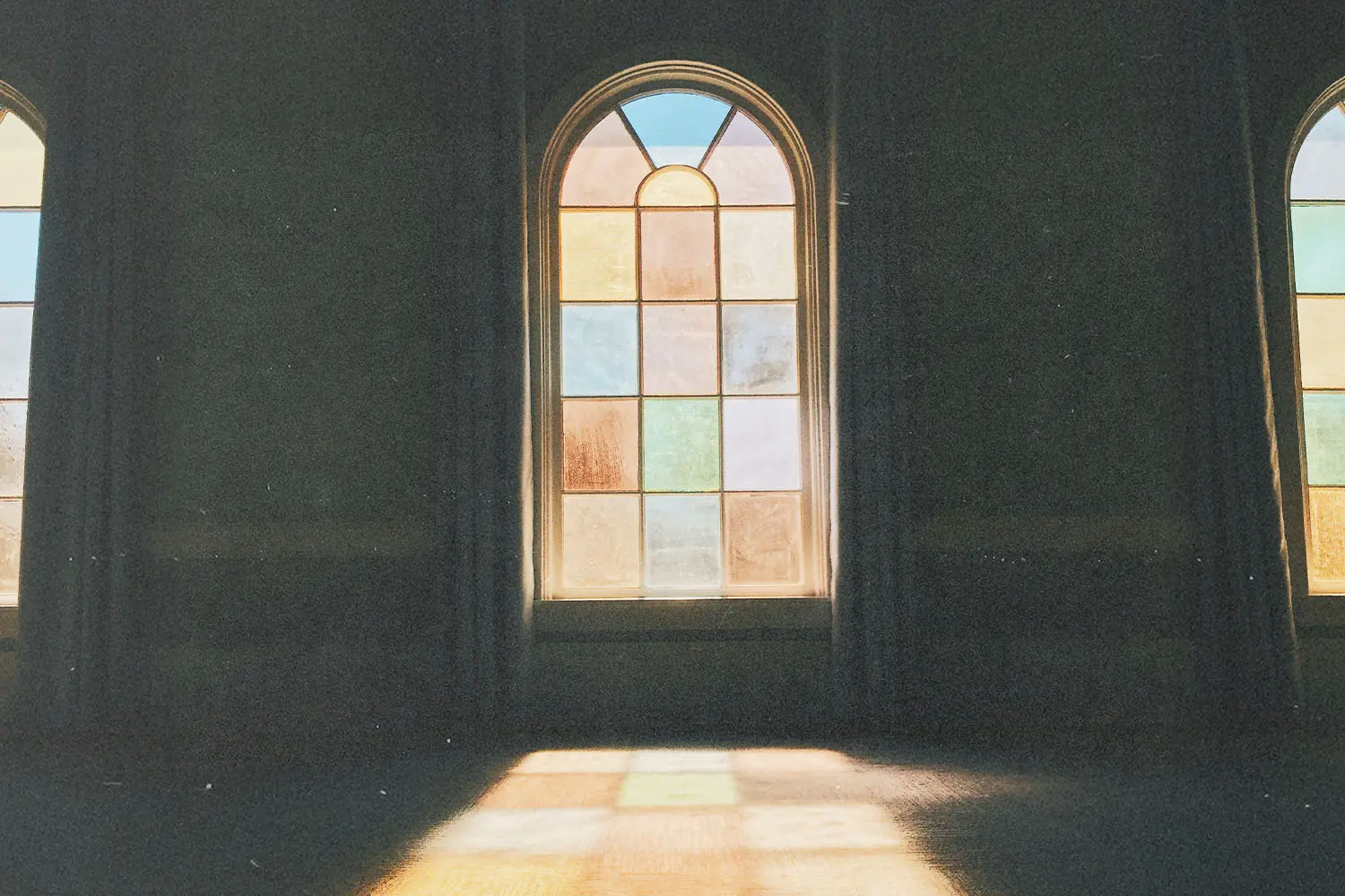 Sunlight shining through tall stained‑glass windows inside a dimly lit room