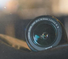 Close-up of a Canon EF‑S zoom lens resting on a dark fabric surface with blurred background lights
