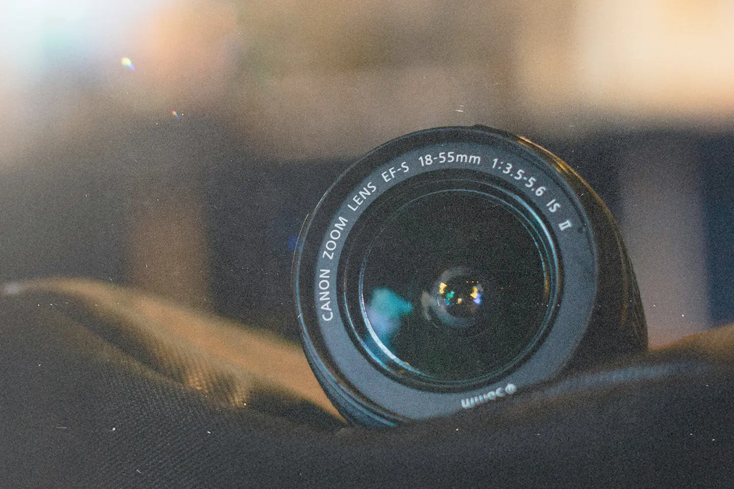 Close-up of a Canon EF‑S zoom lens resting on a dark fabric surface with blurred background lights