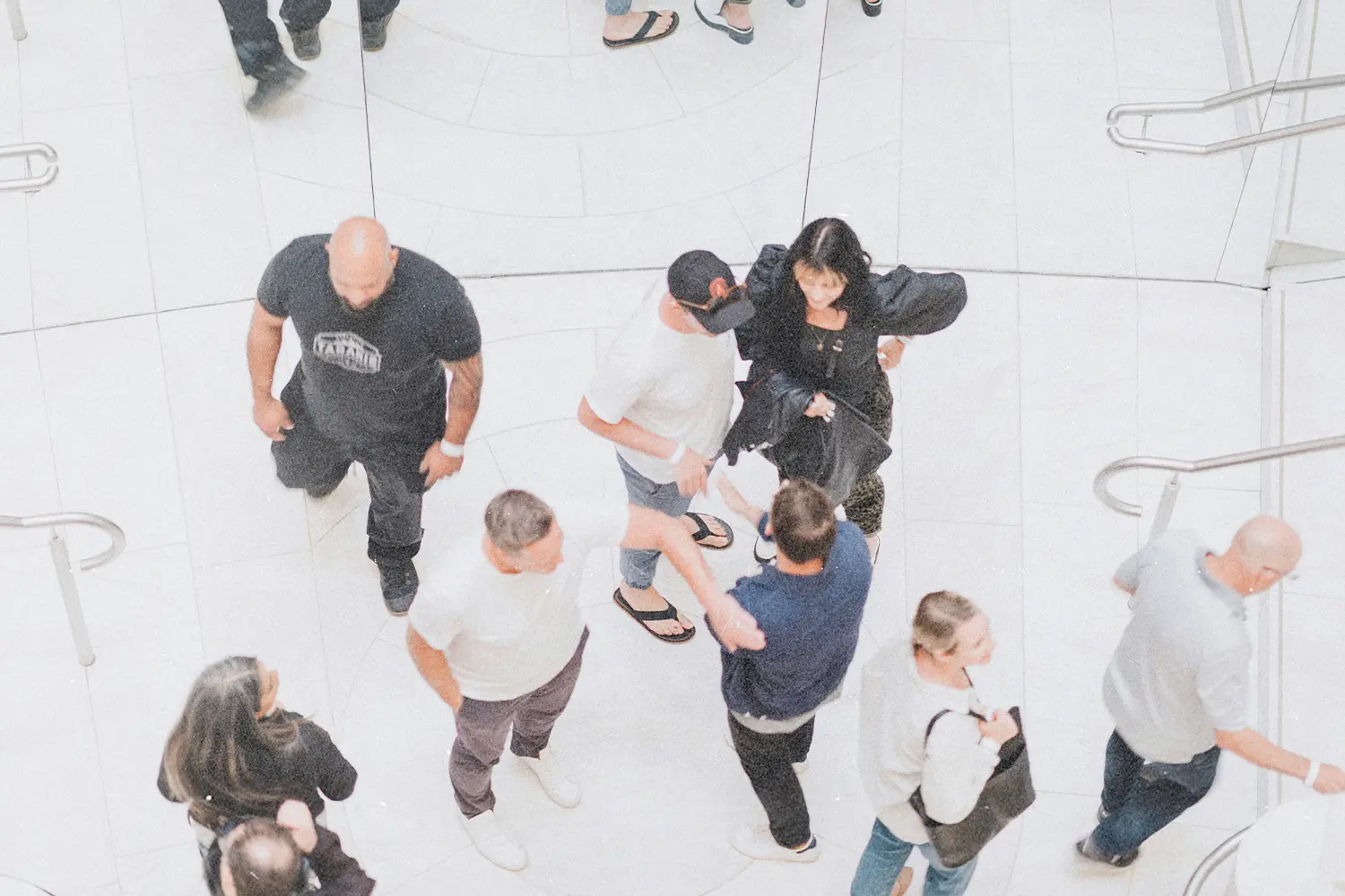 Group of people walking and interacting in a bright, modern indoor mall with white tile floors and metal railings