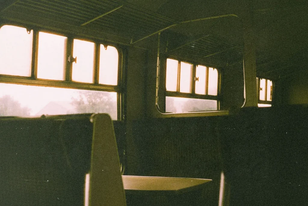 Empty train seats and sunlit windows inside an old-fashioned railway carriage, with warm light filtering through the glass