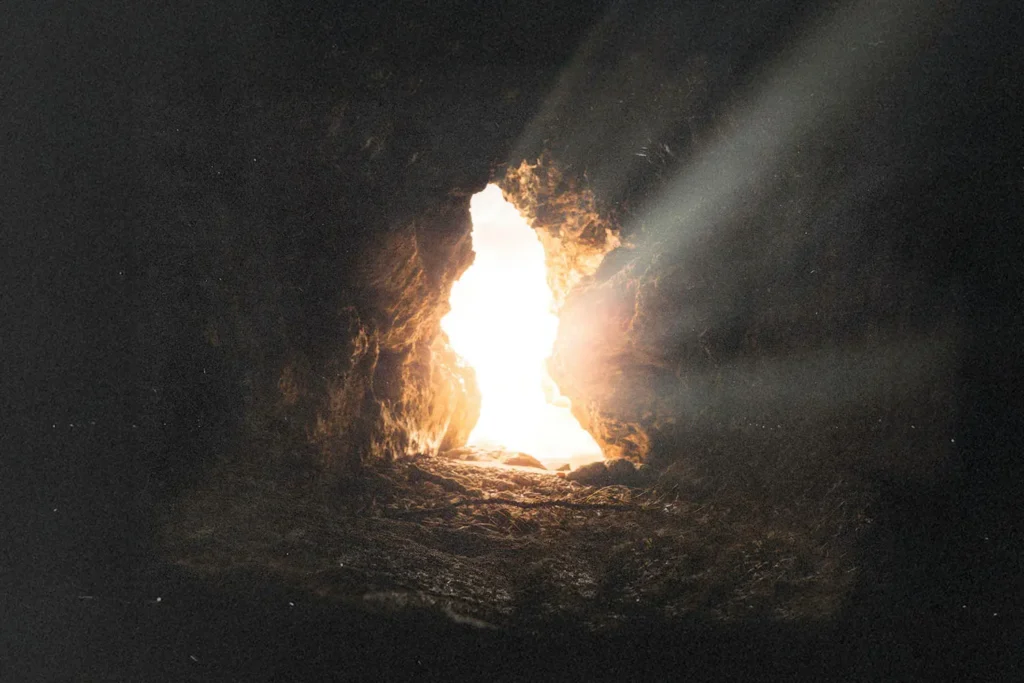 Sunlight streaming through the opening of a rocky cave, illuminating the stone floor with bright, warm rays