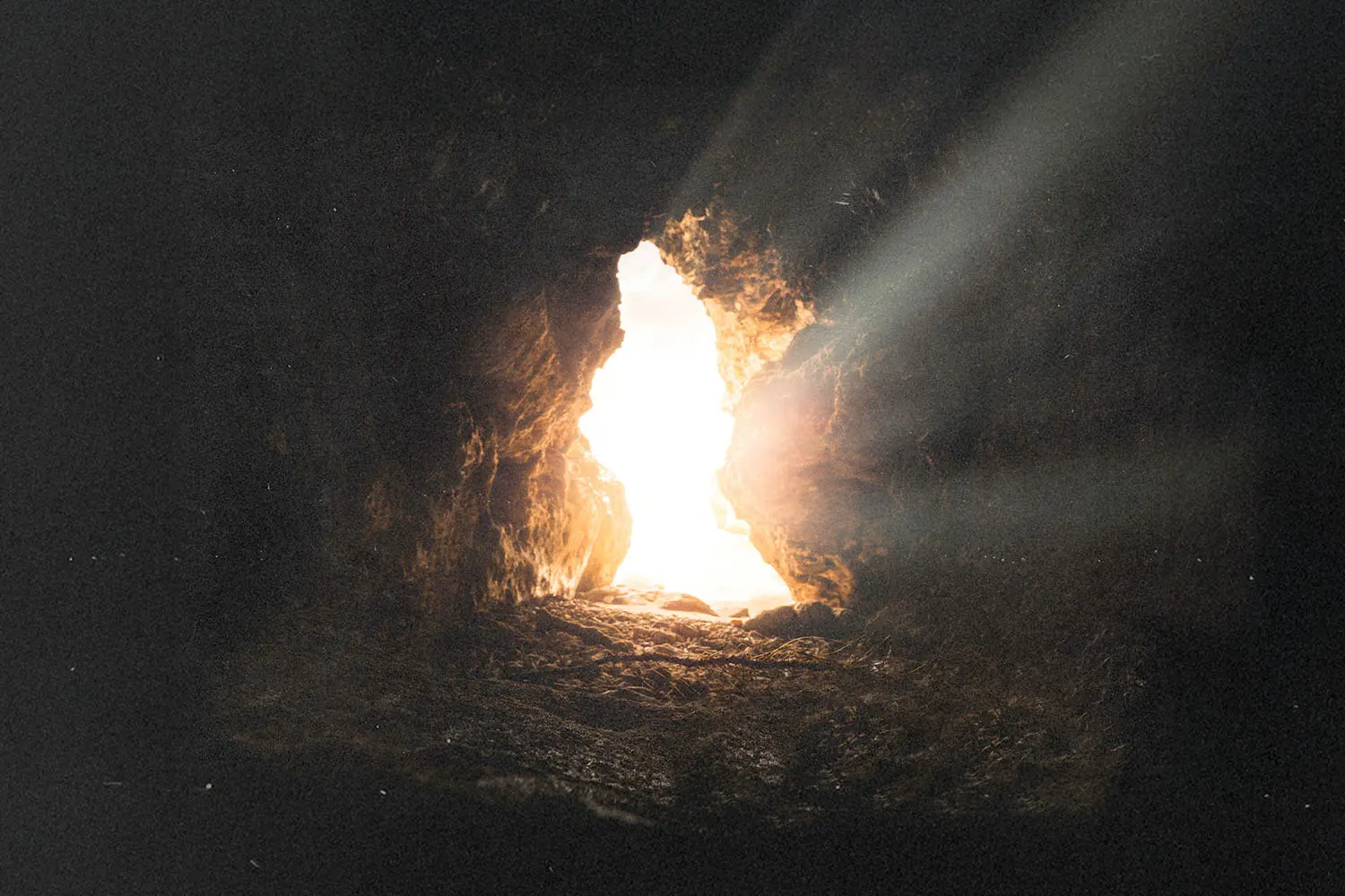 Sunlight streaming through the opening of a rocky cave, illuminating the stone floor with bright, warm rays