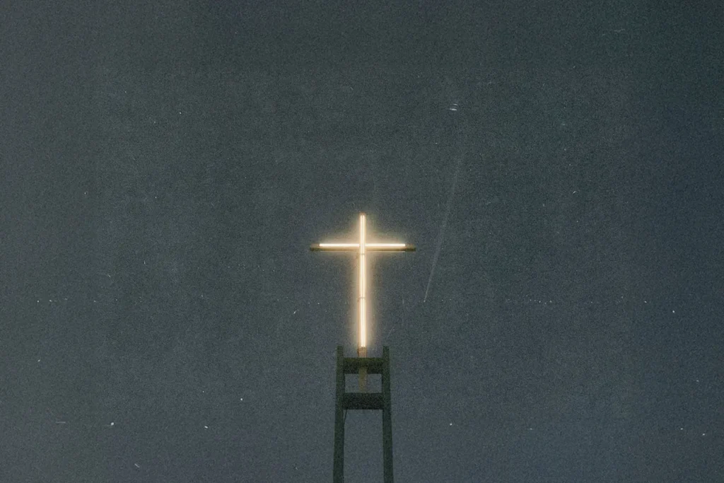 Illuminated cross glowing atop a tall church structure against a dark night sky