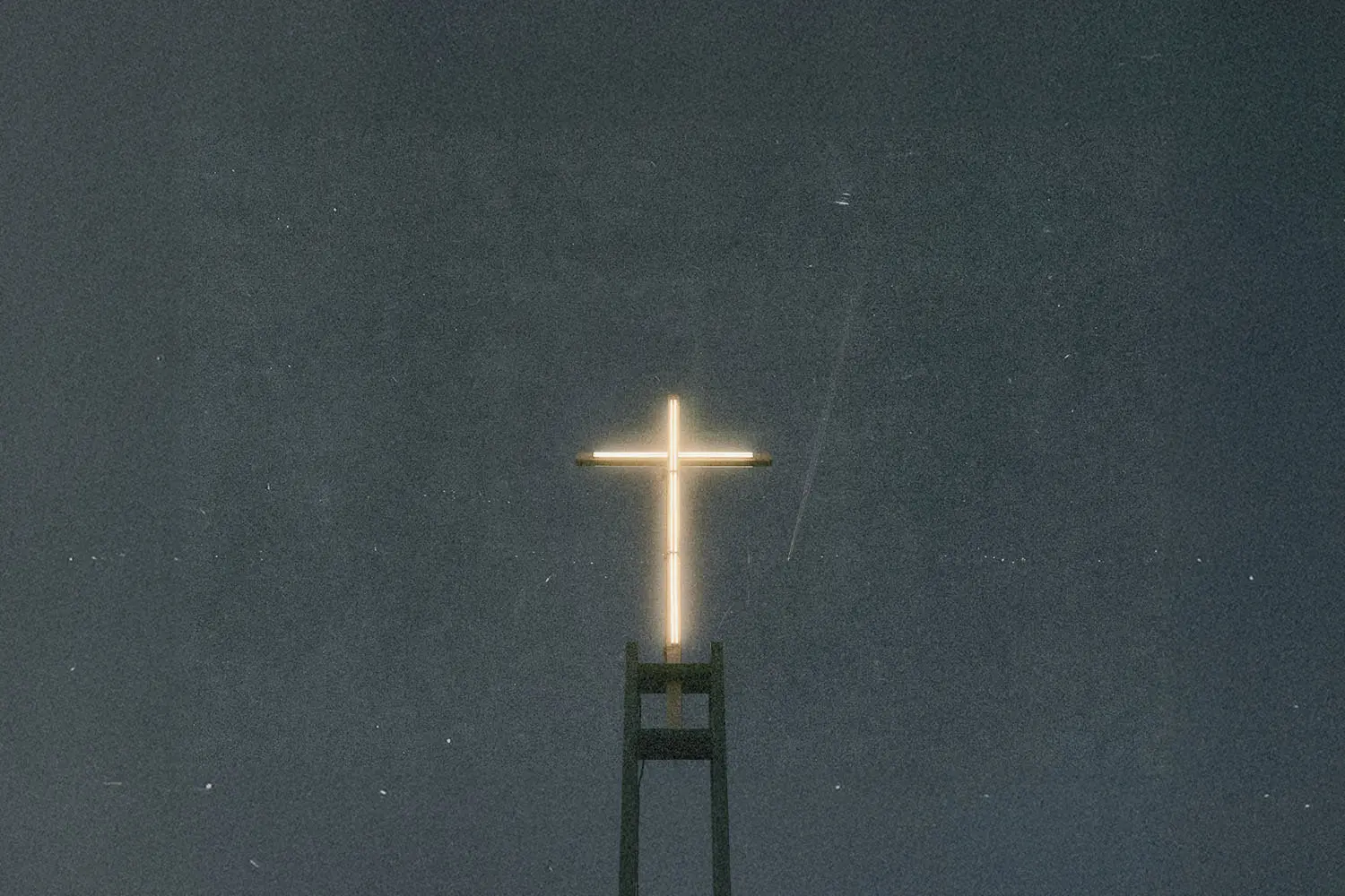 Illuminated cross glowing atop a tall church structure against a dark night sky