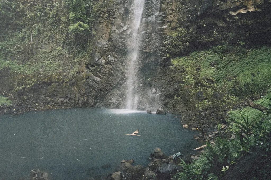 Waterfall flowing into a blue pool with a person swimming below