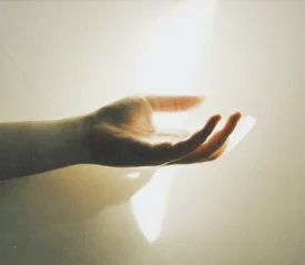 Outstretched hand reaching toward a bright beam of light against a softly lit wall