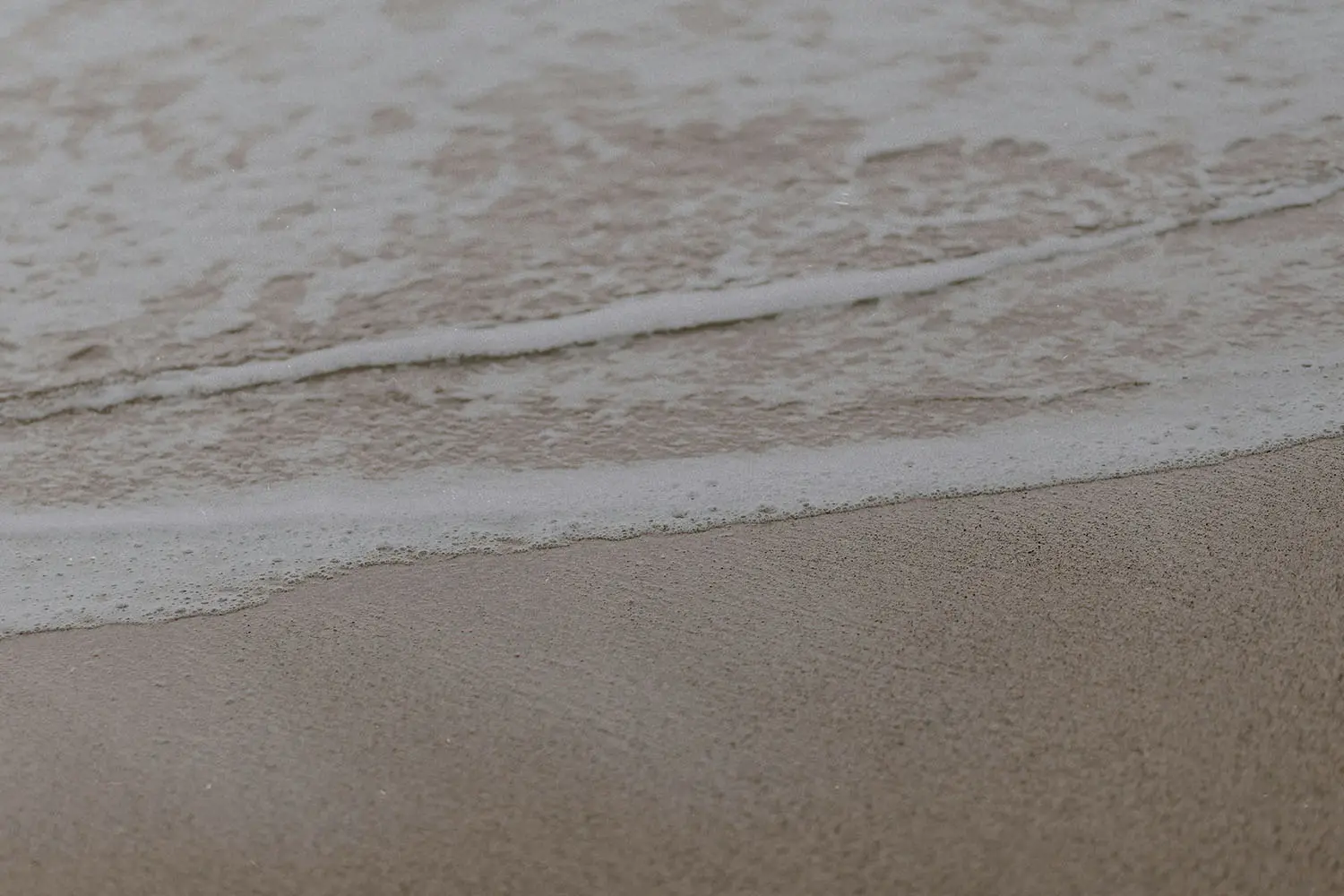 Gentle ocean waves roll onto smooth, wet sand in soft, muted lighting