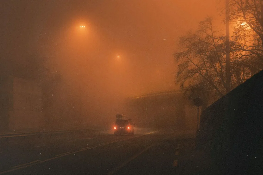 Vehicle driving through dense nighttime fog under glowing overhead lights