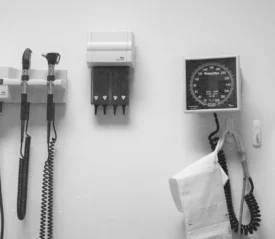 Wall-mounted medical equipment, including an otoscope, blood pressure gauge, and storage units, arranged neatly in a clinical exam room