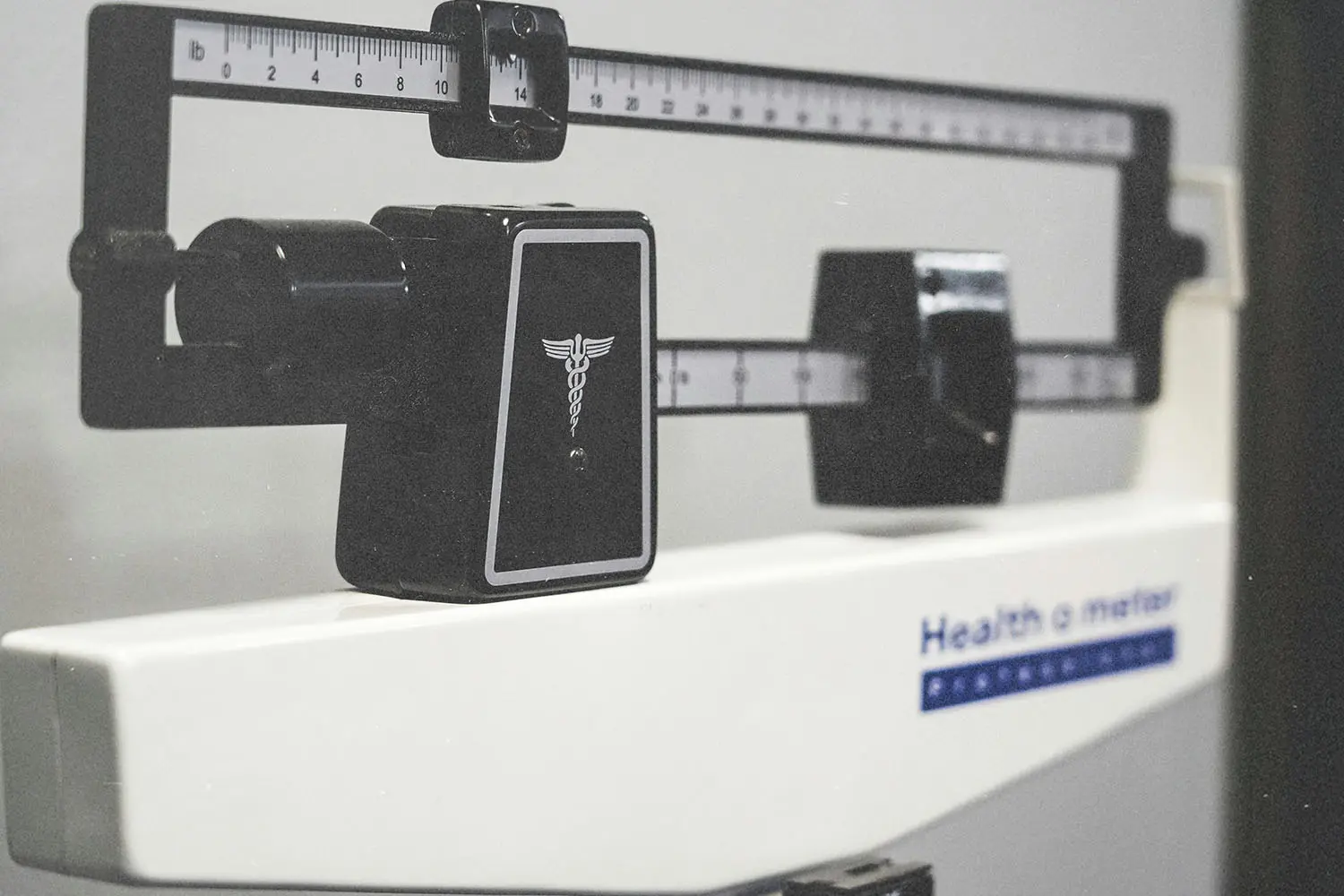 Close-up of a medical beam balance scale with measurement sliders and a caduceus symbol on the front