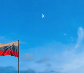 Russian flag waving against a bright blue sky with the moon visible.