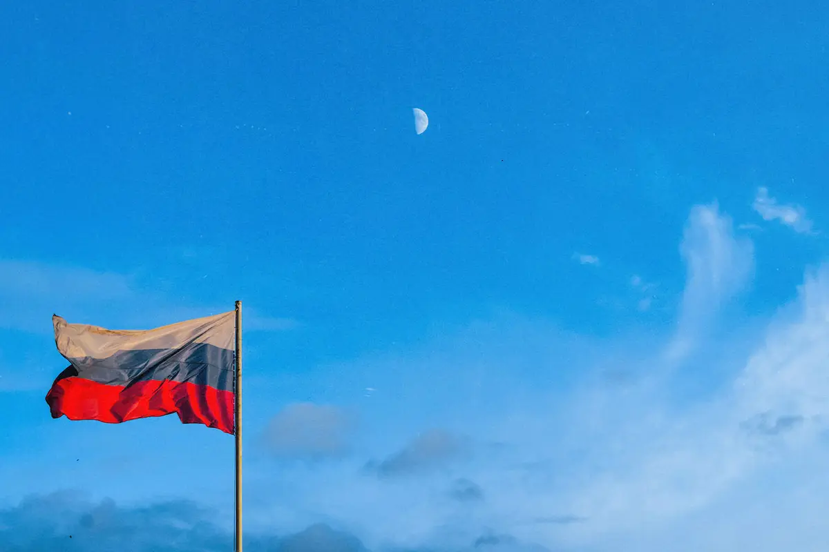 Russian flag waving against a bright blue sky with the moon visible.