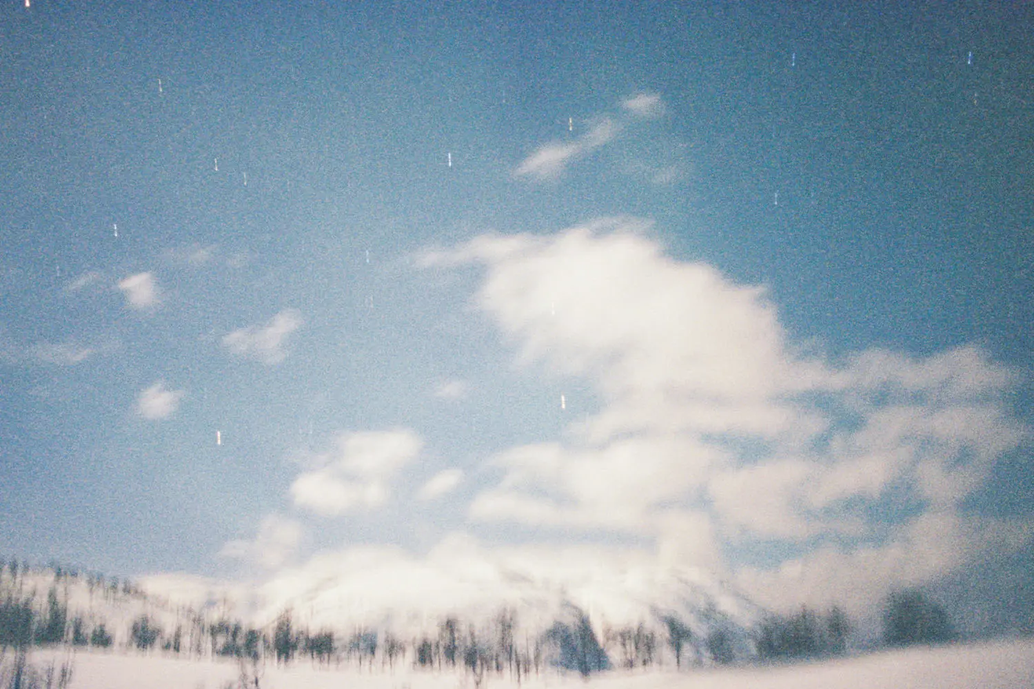 A snowy landscape stretches across the scene under a bright, cloud‑filled sky with faint streaks of stars above