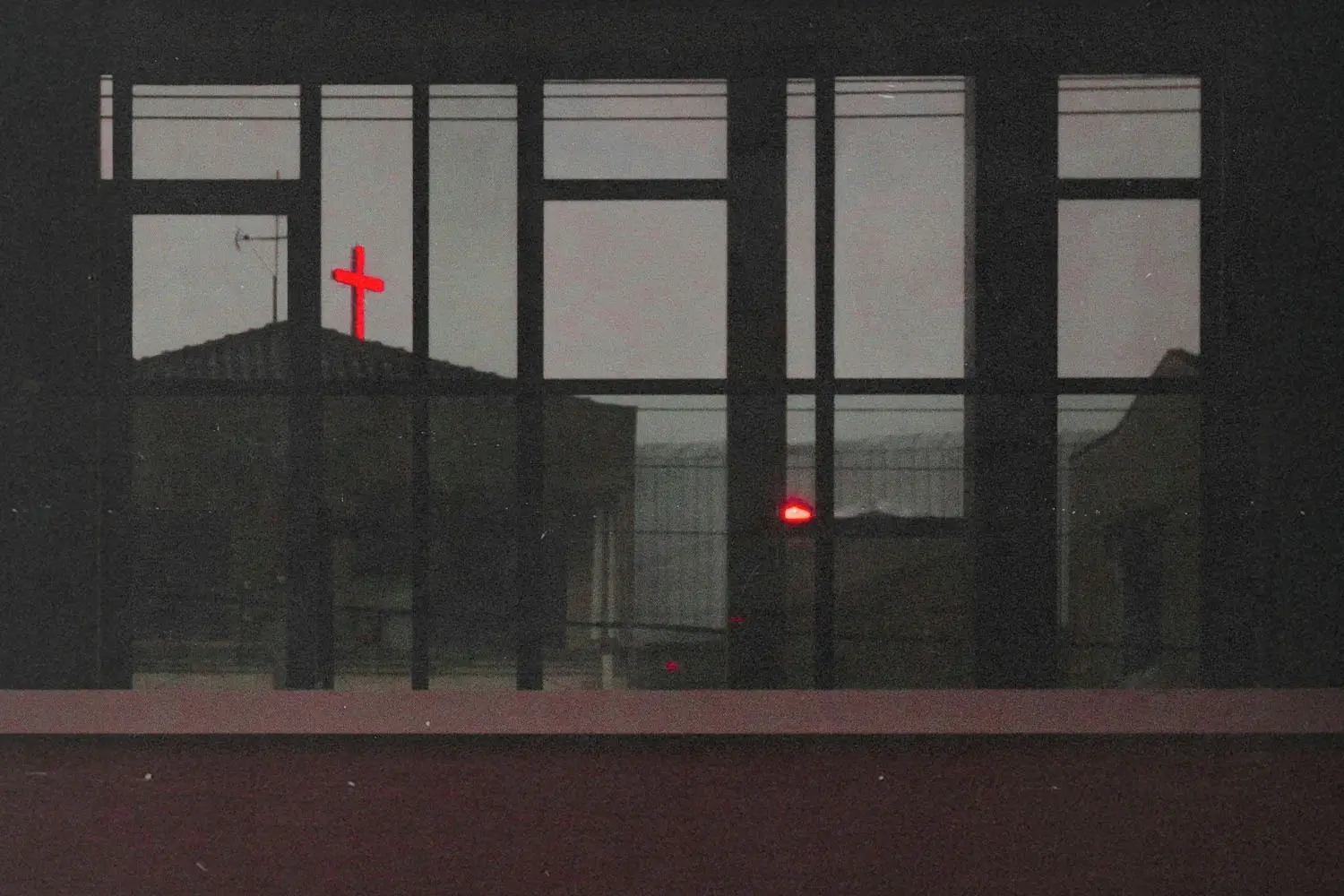 View from a window of a neon red cross atop a building in the distance