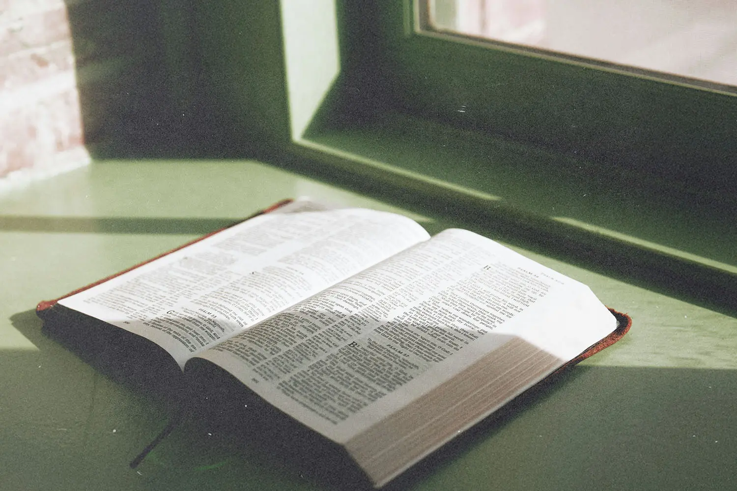 An open Bible rests on a windowsill, lit by soft natural light streaming through a nearby window