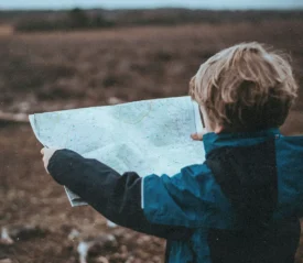Little boy standing in an open field holding a map out in front of him