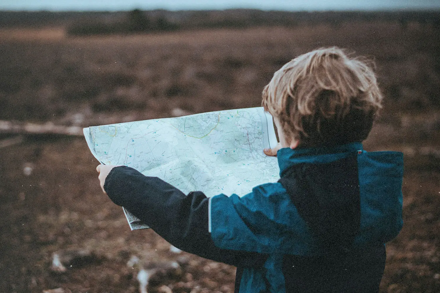 Little boy standing in an open field holding a map out in front of him