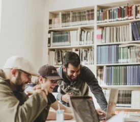 Group of men smiling and laughing around a laptop screen