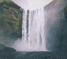 Powerful waterfall cascading down a moss-covered cliff into a misty pool below