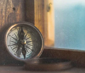 A compass rests on a wooden windowsill, lit softly by warm natural light