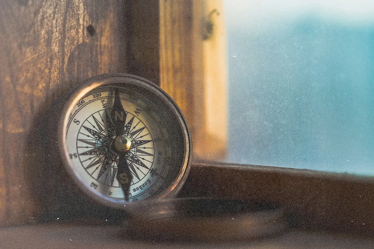 A compass rests on a wooden windowsill, lit softly by warm natural light