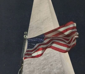 An American flag waves at night in front of a tall stone monument, illuminated from below