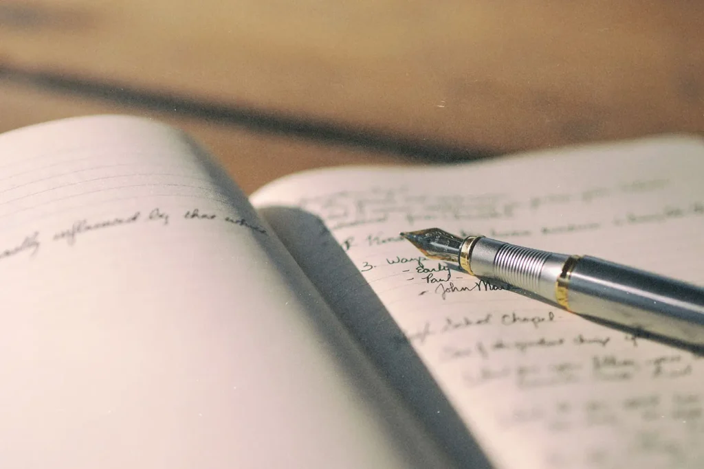 A fountain pen rests on the open pages of a notebook filled with handwritten notes, lit by warm natural light