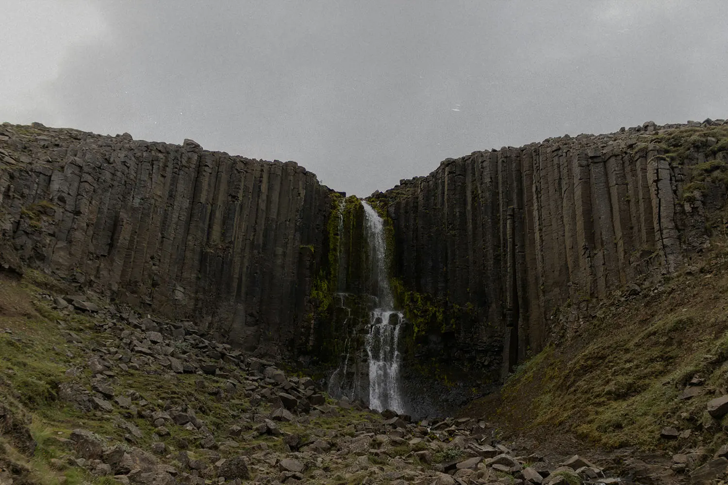 Tall waterfall cascading through a narrow gap between vertical basalt rock columns