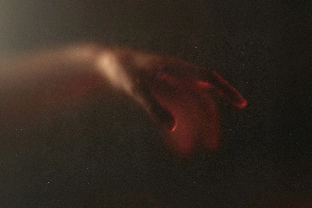 Softly lit hand reaching out in a dark, shadowy environment with a warm red glow along the fingers