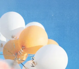 White and golden balloons rising toward a cloudless blue sky