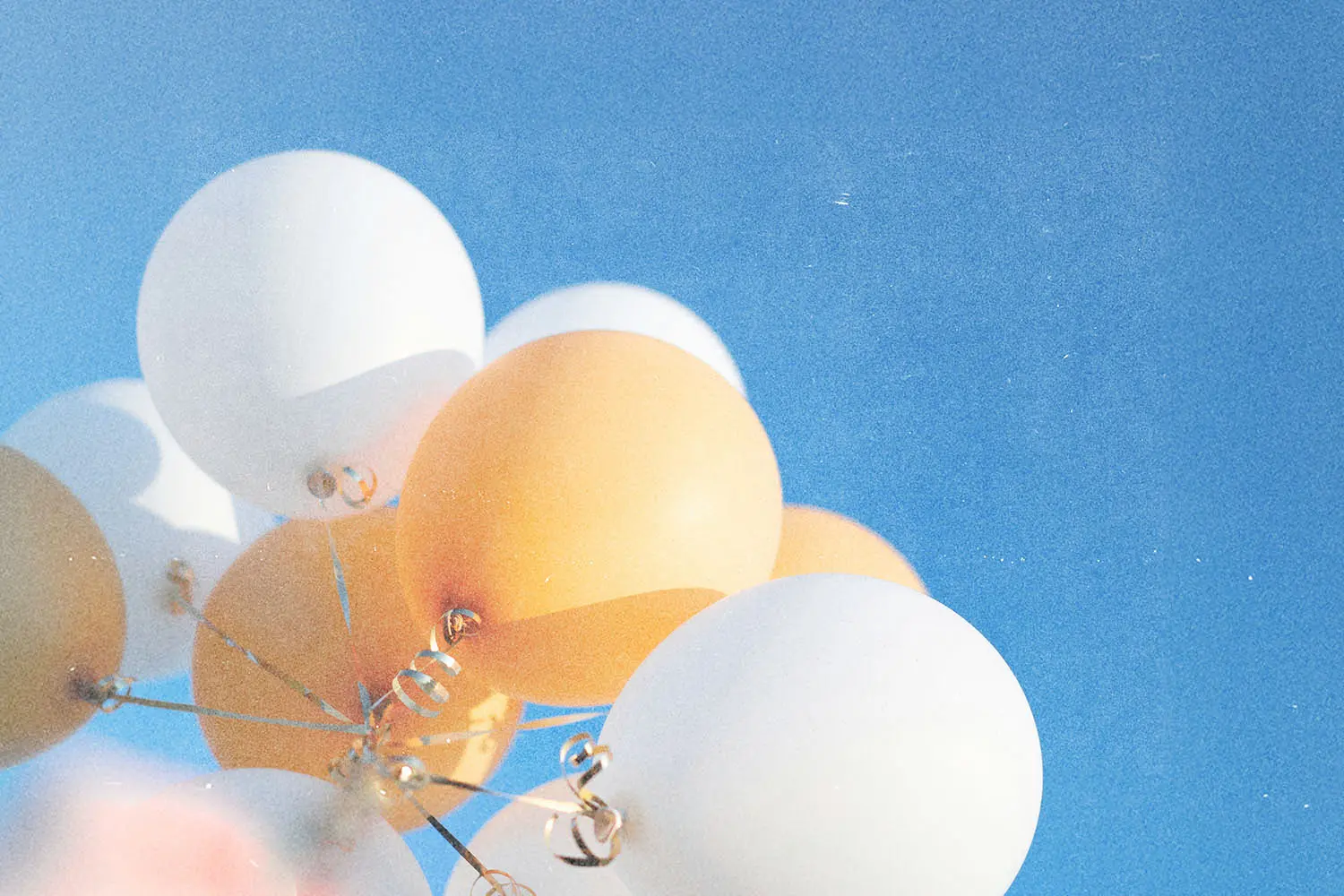 White and golden balloons rising toward a cloudless blue sky